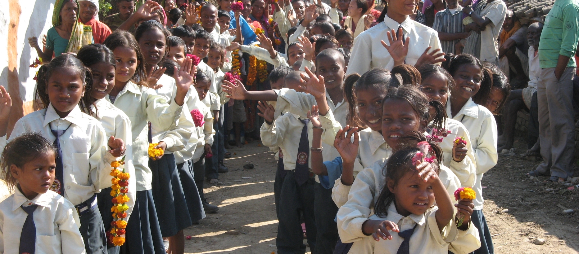 Nepalin lapsia pukeutuneena koulupukuihin seisomassa jonoissa ja vilkuttavat kameralle.
