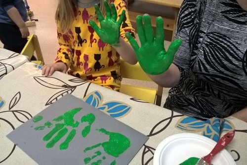 Lapsen ja mummon kämmenet ovat vihreänä väristä, kun käsien kuvan painaminen paperille on saatu päätökseen.